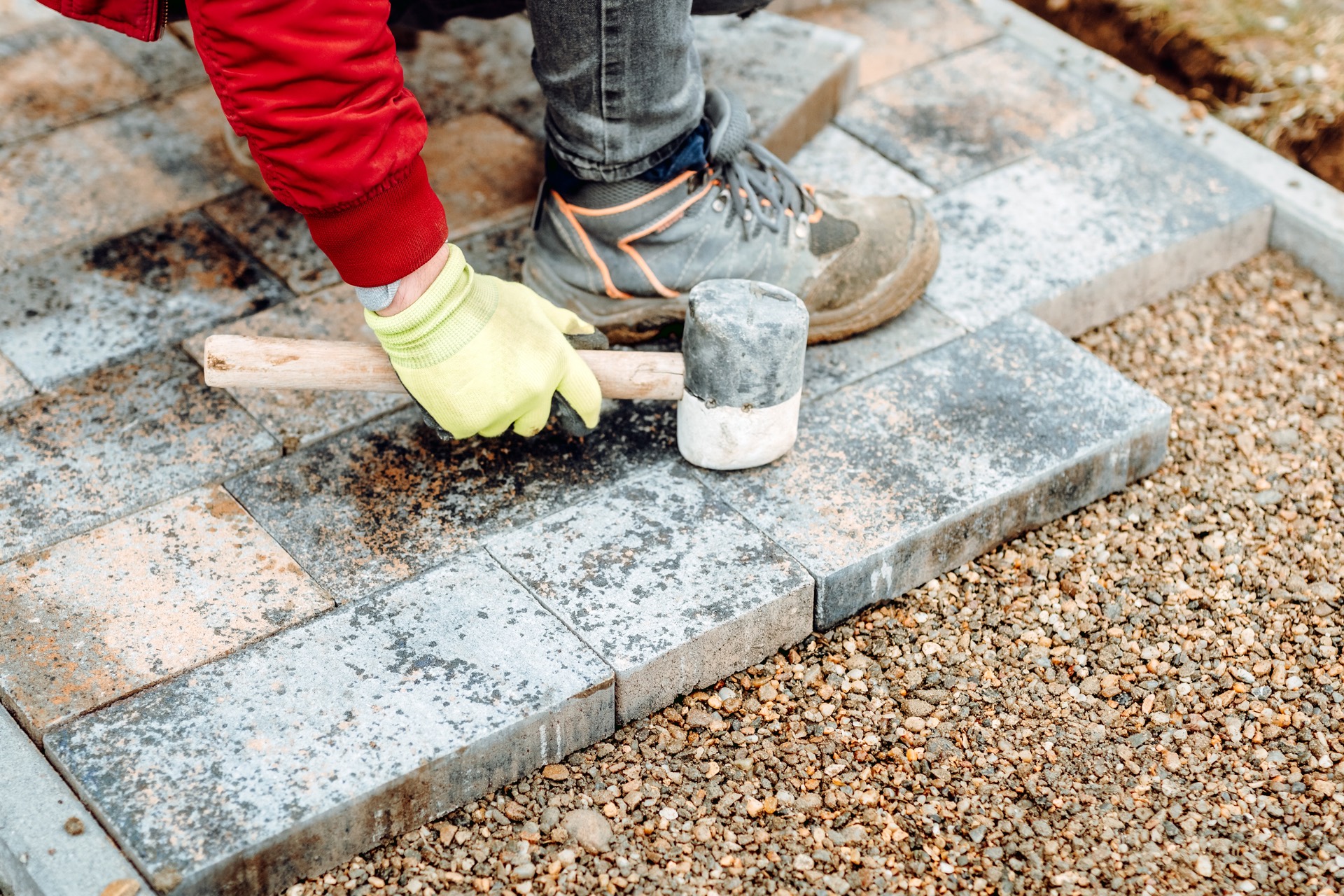 A worker setting interlocking decorative pavers in fresh sand